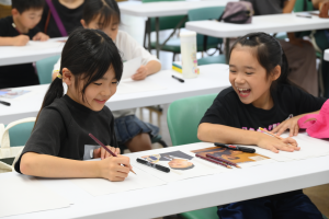 児童2人が楽しそうに似顔絵を描いている様子
